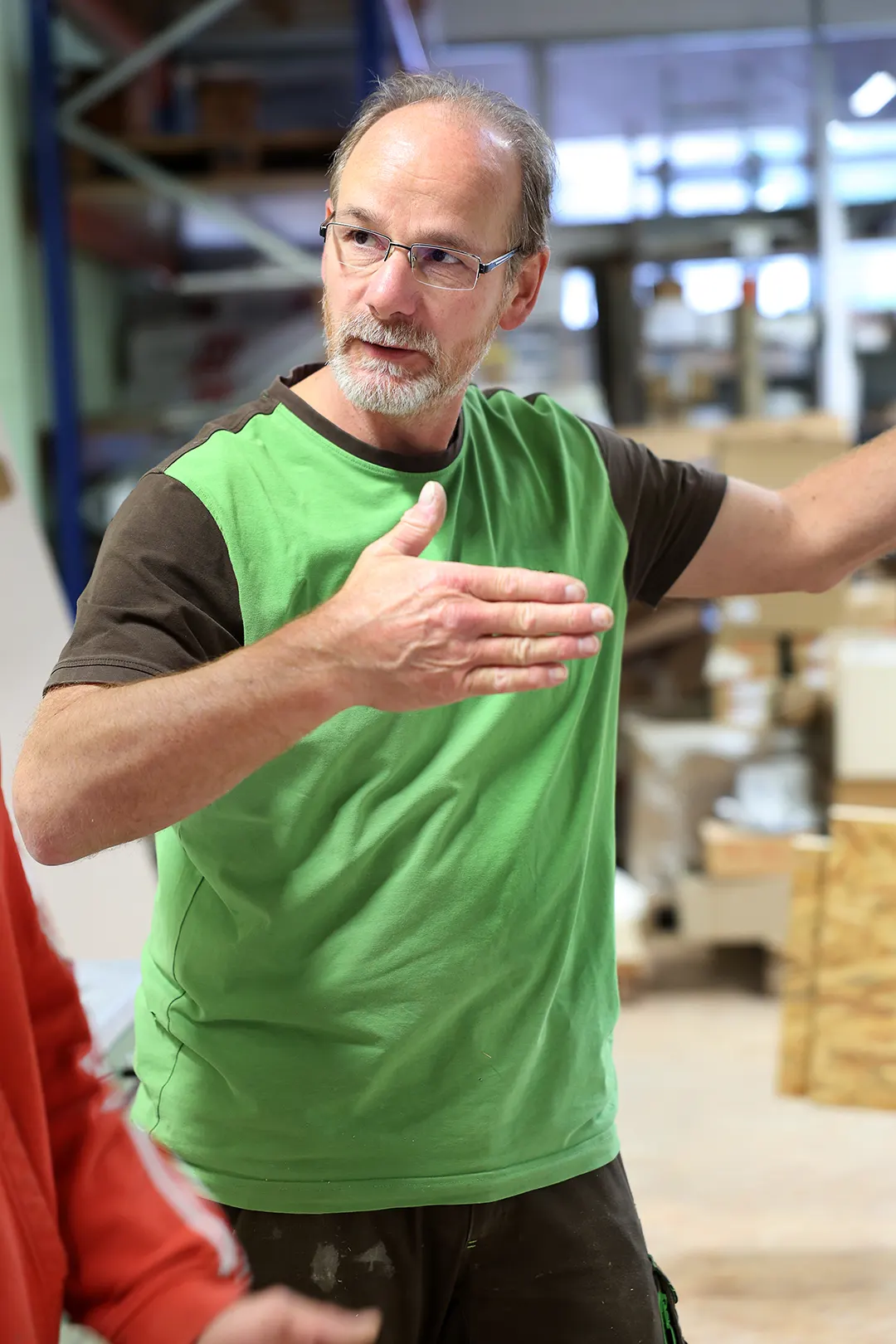 Handwerker mit Brille erklärt Arbeitsschritte in einer modernen Werkstatt für Holzverarbeitung.