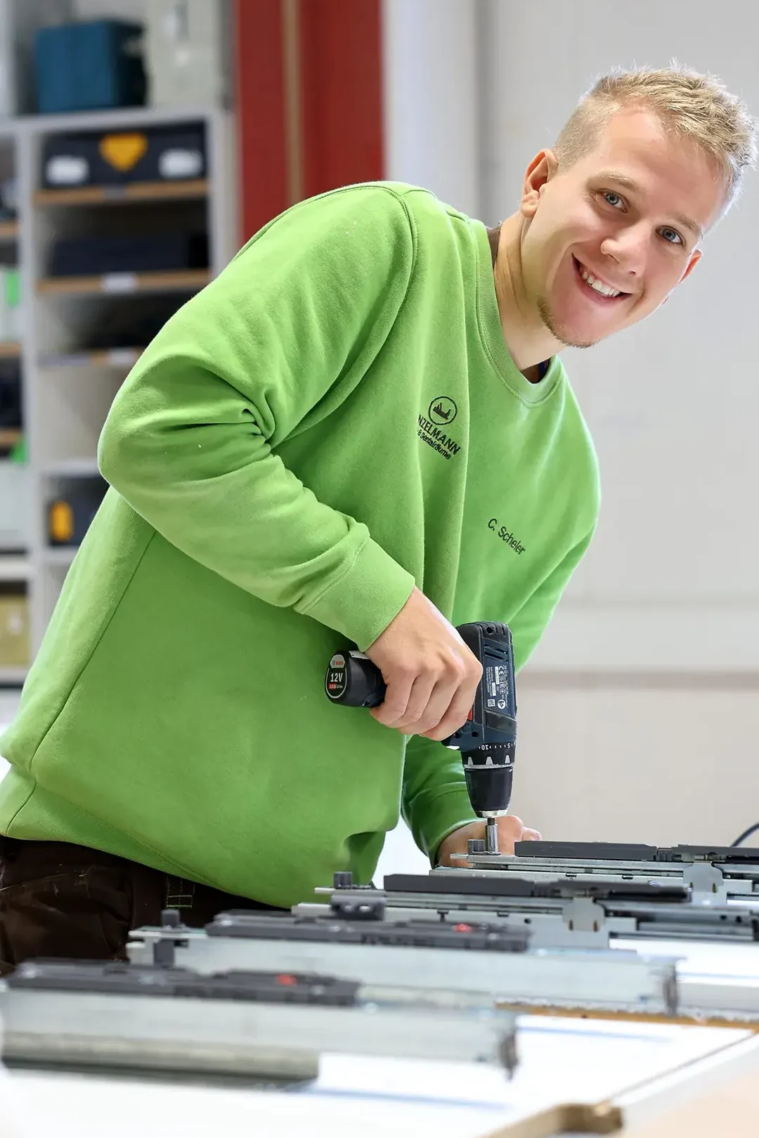 Junger Handwerker arbeitet lächelnd mit Akkuschrauber in moderner Werkstatt.